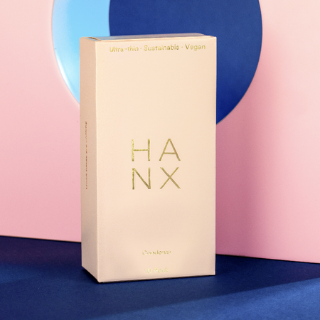 HANX natural, ultra-thin Condoms in a cream and gold detailed box, against a pink and blue sculptural background