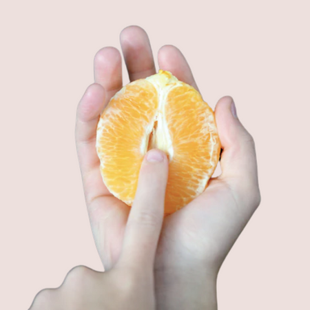 White hand holding an orange suggestively as a metaphor for a vagina.