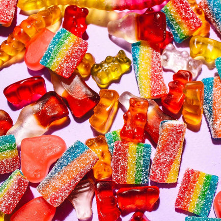Sugar covered rainbow sweeties and gummy bear candies are tumbled on a pink background