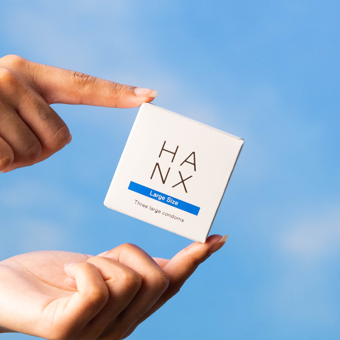 A HANX Vegan large size condom 3 pack being held between two fingers.