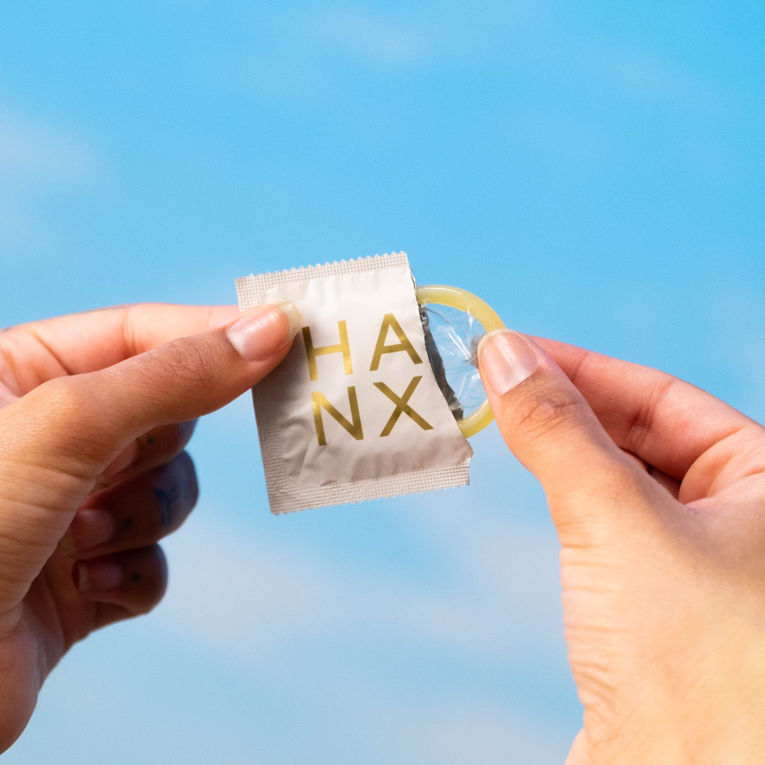 A HANX condom packet half open, with the condom being removed from the inside.