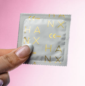 The gold and white wrapping of one of HANX's vegan, sustainable, biodegradable condoms held by a manicured hand.