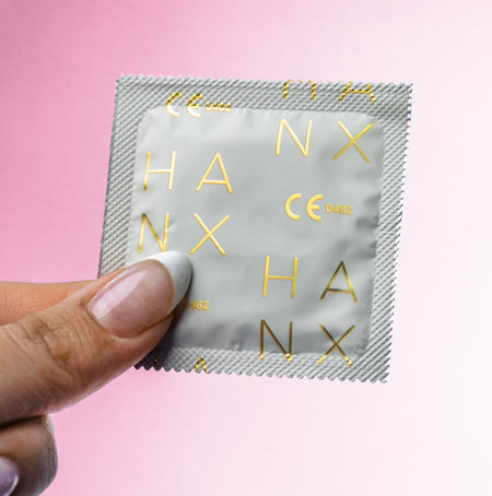 The gold and white wrapping of one of HANX's vegan, sustainable, biodegradable condoms held by a manicured hand.