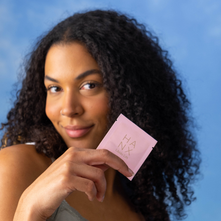 A woman smiling and holding a packet of HANX's natural libido supplement for women, HANX Libido Lift.